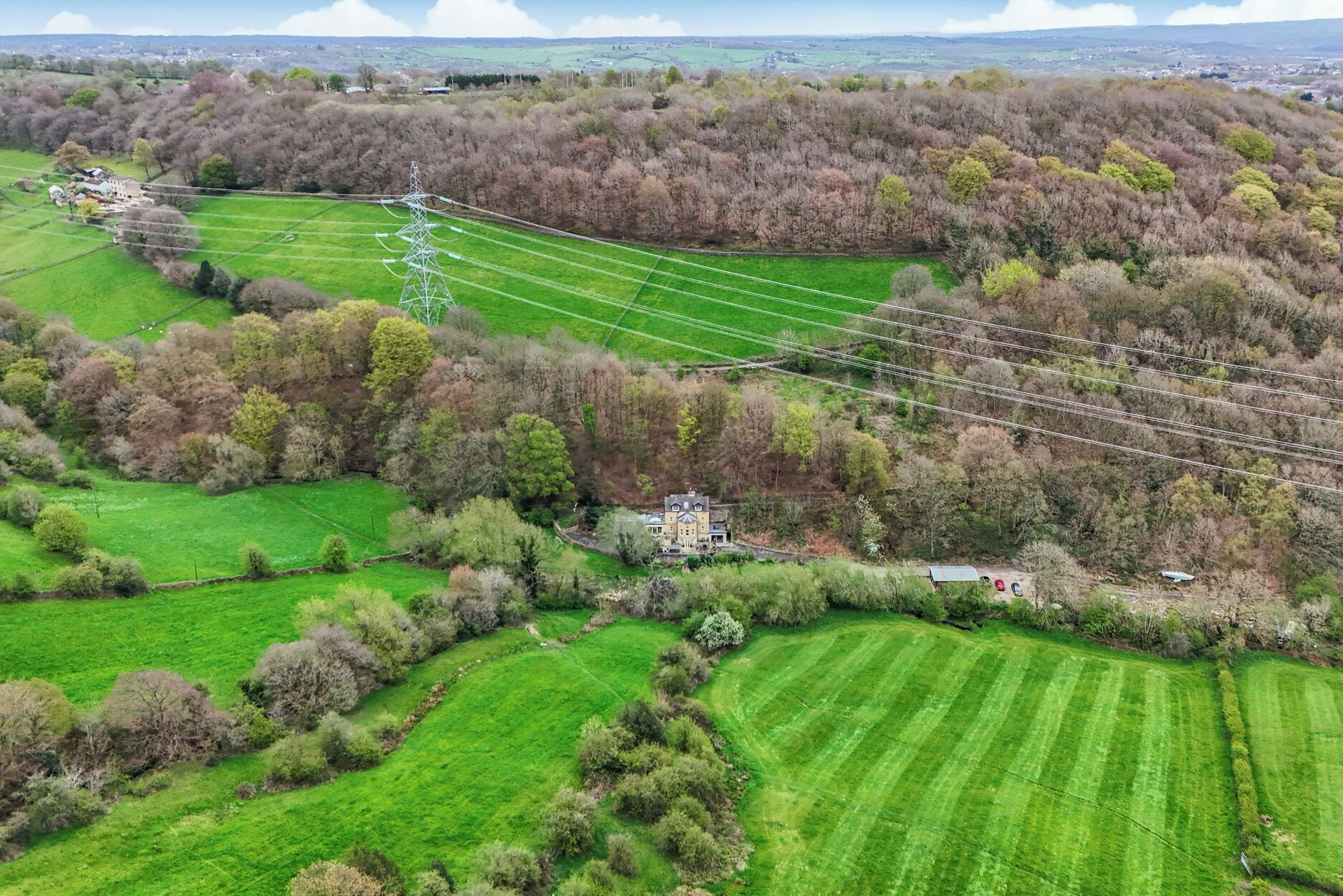 Vista aérea de un paisaje rural con una gran propiedad, líneas eléctricas y campos verdes.