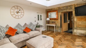 A modern living room with a high ceiling, a large clock, a sofa set, a console table, and a herringbone wooden floor. - Belvedere Farm (Halifax)