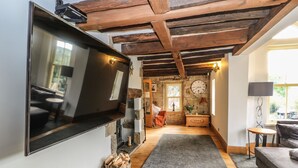 A cozy living room with a flat-screen TV, wooden beams, a stone wall, a clock, and a small side table labeled 'TOYS'. - Belvedere Farm (Halifax)