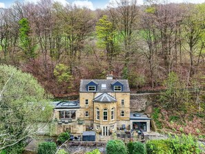 A large stone building with multiple windows and a prominent entrance, surrounded by dense trees and a small water feature. - Belvedere Farm (Halifax)
