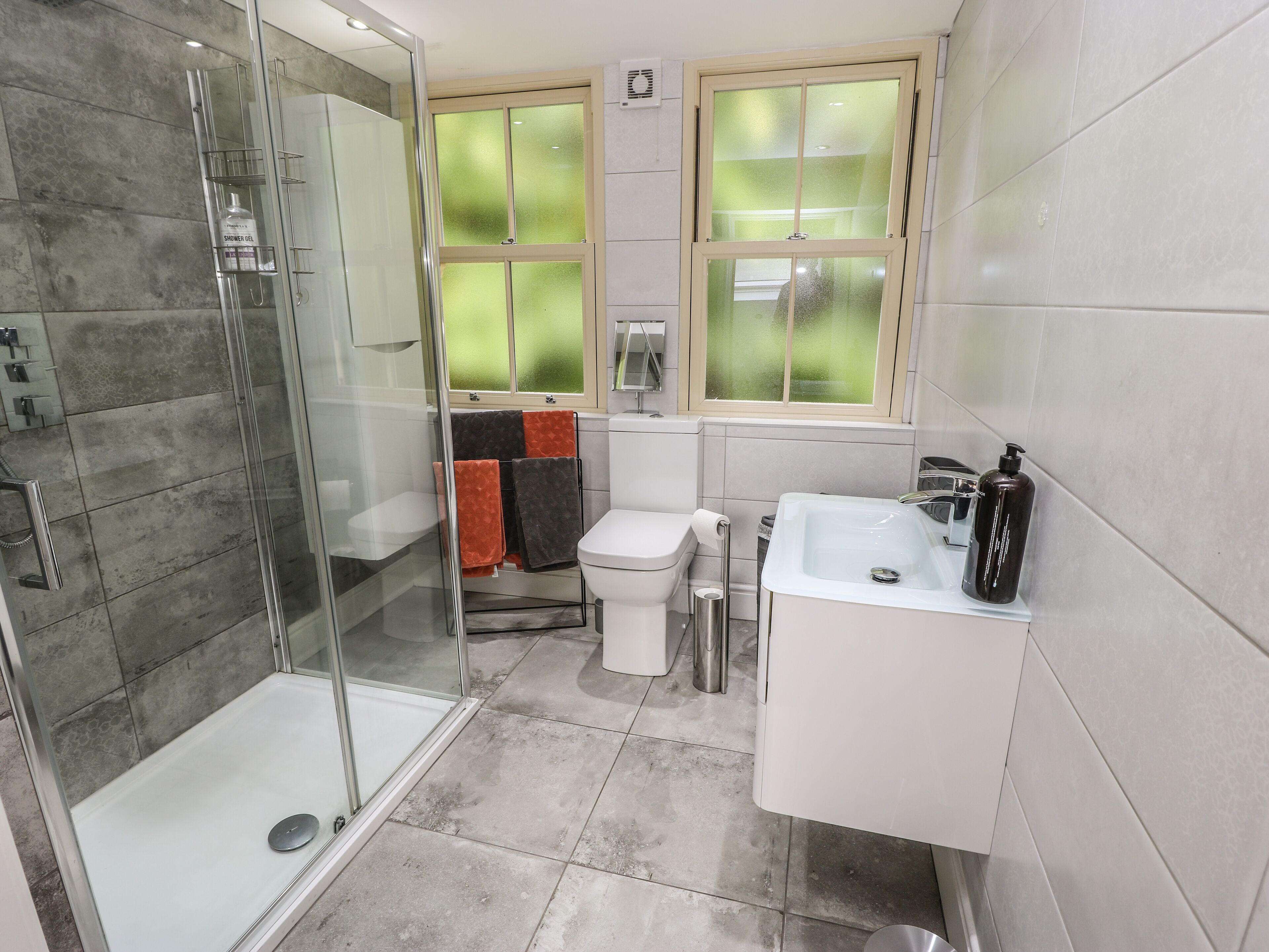 Een moderne badkamer met een douchecabine van glas, een toilet, een wastafel en een raam met gezandstraald glas.