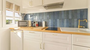 Uma cozinha com armários brancos, painel de azulejos azuis, micro-ondas, torradeira e pia com torneira dourada.