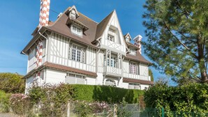 Uma casa grande de dois andares com telhado inclinado, várias chaminés e fachada xadrez branca e vermelha.