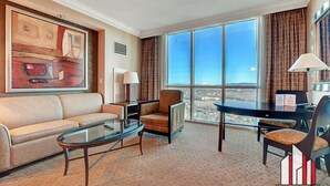A hotel room with a large window, a sofa, a glass coffee table, and a chair. - Floor-to-Ceiling Jacuzzi Studio | The Signature (Las Vegas)