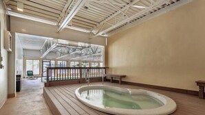 Una amplia piscina cubierta con terraza de madera, una banca y vistas al exterior a través de grandes ventanales.