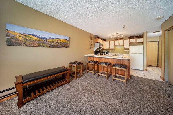 A compact kitchen with a bench and stools, a refrigerator, and a microwave.