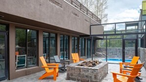 Un patio exterior moderno con suelo de piedra, una chimenea y sillas Adirondack color naranja.