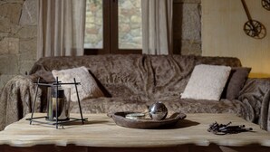 Une pièce chaleureuse avec un mur en pierre, une table en bois, un canapé avec des coussins et une fenêtre avec des rideaux.