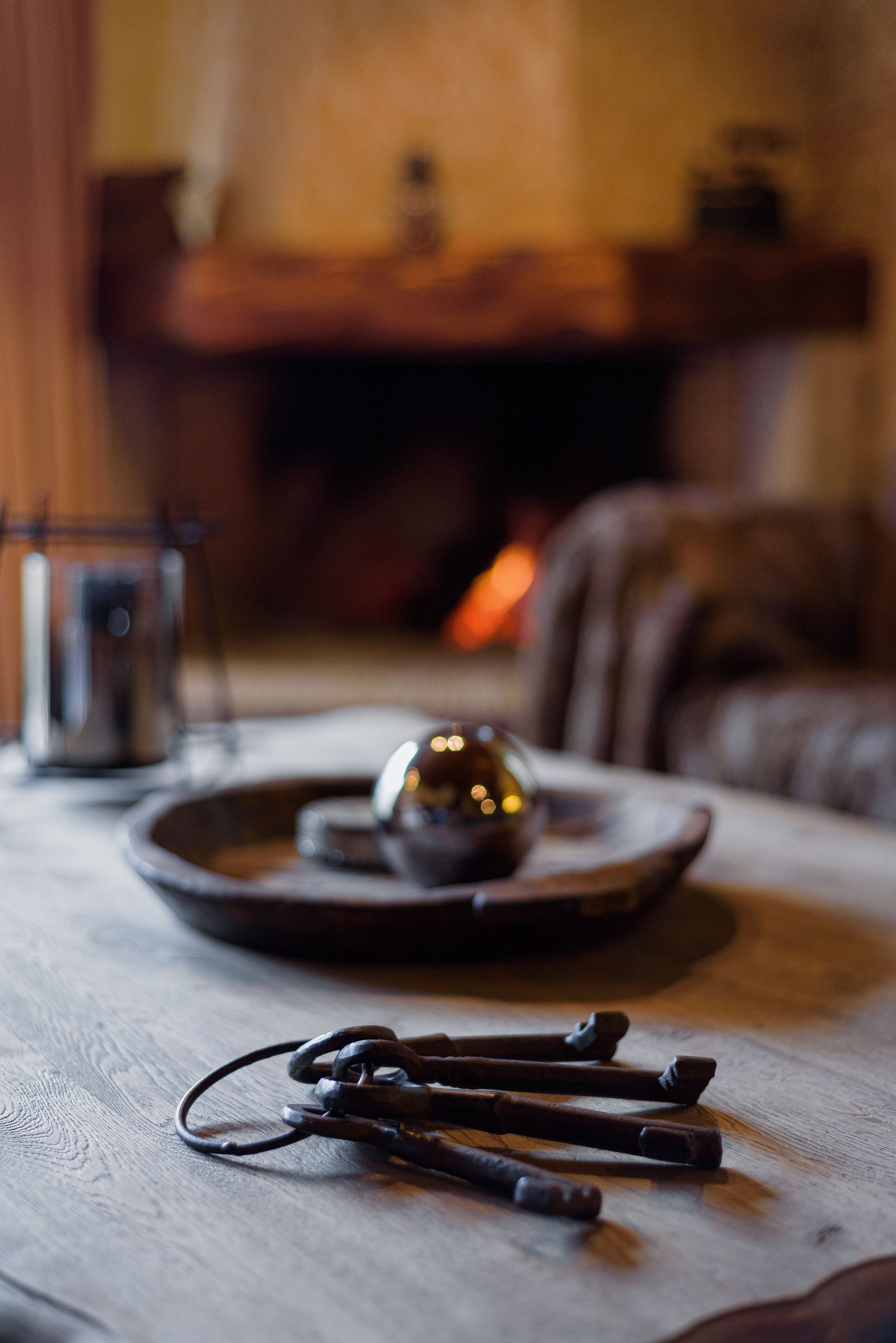 A wooden table with a glass candle holder, a metal candle holder, and a tray with a spherical object.