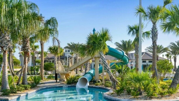 Una piscina con tobogán de agua, rodeada de palmeras y un edificio al fondo.