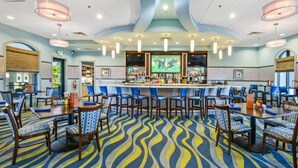 Un vestíbulo de hotel con área de bar, arreglos de asientos y alfombra estampada.