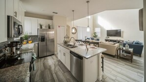Una cocina moderna con una isla central, electrodomésticos de acero inoxidable y un comedor con sofá y televisor.