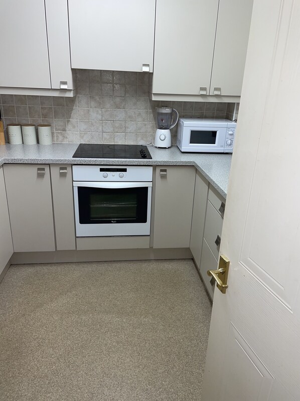 A kitchen with white cabinets, a built-in oven, a microwave, and a blender on the countertop.