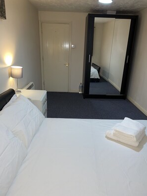 A hotel room with a bed, a bedside table, a lamp, a mirror, and a door.