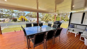 A covered outdoor area with a wooden deck, a table with chairs, and a sofa. - Barefoot and Beach Bound by Book Jervis Bay (Vincentia)