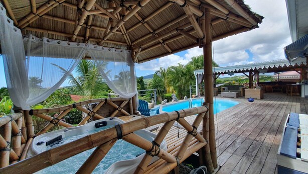 A bamboo-framed outdoor pool area with a hot tub, lounge chairs, and a covered seating area.