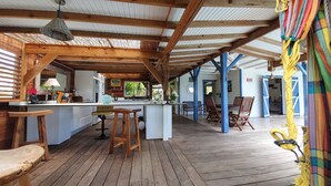 A spacious covered patio with wooden flooring, a central island with bar stools, and a dining area with chairs.