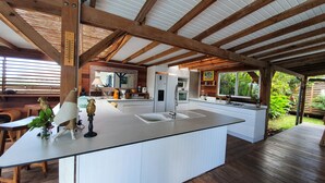 A modern kitchen with a large island, wooden beams, and a view of the garden.
