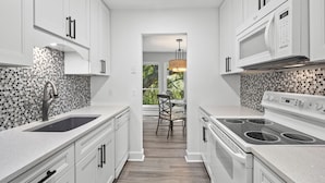 A modern kitchen with white cabinetry, a granite countertop, a stainless steel sink, a built-in oven, and a microwave. - Third floor Sea Pines villa overlooking the lagoon, minutes from Harbour Town (Hilton Head Island)