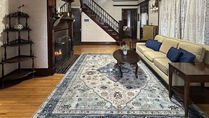 A living room with a sofa, coffee table, patterned rug, fireplace, and a staircase.