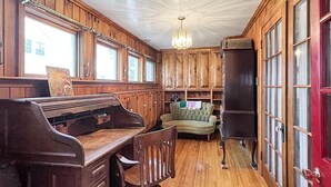A room with wooden paneling, a piano, a green sofa, and a red door.