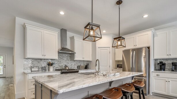 A modern kitchen with white cabinetry, a marble countertop, a stainless steel refrigerator, and wooden bar stools. - Convenient Location to Beach & Downtown (Hilton Head Island)