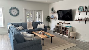 A living room with a blue sofa, a wooden coffee table, a TV, and a bookshelf. - Convenient Location to Beach & Downtown (Hilton Head Island)
