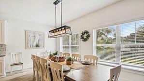 A dining area with a wooden table, white chairs, and a hanging light fixture. - Convenient Location to Beach & Downtown (Hilton Head Island)