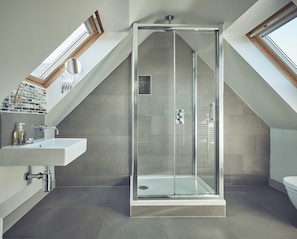 Un baño moderno con cabina de ducha de vidrio, un lavabo blanco y un tragaluz.