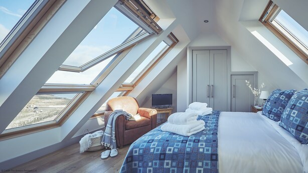 A bedroom with a large bed, a chair, a TV, and a wardrobe. There are skylights providing natural light. - Craster Reach -  a family friendly that sleeps 6 guests  in 3 bedrooms (Alnwick)