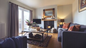 A cozy living room with a fireplace, a comfortable sofa, a coffee table, and a television. - Craster Reach -  a family friendly that sleeps 6 guests  in 3 bedrooms (Alnwick)