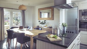 A modern kitchen with a large island, stainless steel appliances, and a dining area with a view of the outdoors. - Craster Reach -  a family friendly that sleeps 6 guests  in 3 bedrooms (Alnwick)