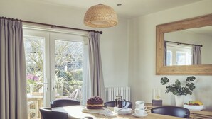 A dining area with a wooden table, black chairs, a hanging light fixture, and a view of the outdoors through large windows. - Craster Reach -  a family friendly that sleeps 6 guests  in 3 bedrooms (Alnwick)
