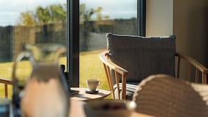 Una habitación con vista al mar, una silla, una mesa con una taza y un ventanal.