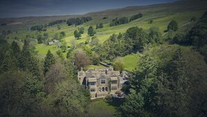 A large, historic stone building surrounded by lush green hills and trees. - Oughtershaw Hall -  a large propertie that sleeps 16 guests  in 8 bedrooms (Skipton)