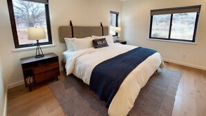 Une chambre à coucher avec un lit, deux tables de chevet, une tête de lit et deux fenêtres.