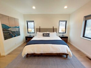 A bedroom with a large bed, two bedside tables, a headboard, and a painting on the wall.