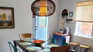 Een eetruimte met een houten tafel, groene stoelen, een hanglamp en een deur met raam.