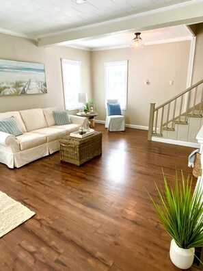 A spacious living room with a wooden floor, a sofa, a chair, a small table, and a staircase. - Steps Away (South Haven)