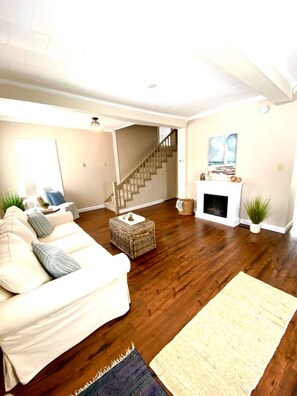 A living room with a white sofa, a fireplace, a staircase, and a large window.