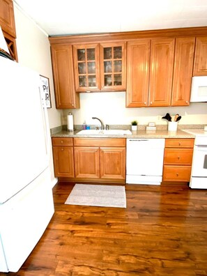 A kitchen with wooden cabinets, a white refrigerator, a sink, and a dishwasher. - Steps Away (South Haven)