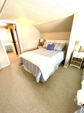 A bedroom with a bed, bedside tables, and a door leading to another room.