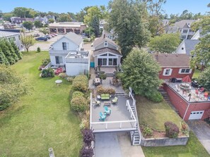 A residential area with a house featuring a deck with outdoor furniture, a lawn, and a garage.
