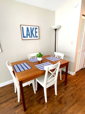 A dining area with a wooden table and white chairs, a potted plant, and a 'LAKE' sign on the wall.