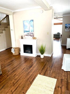 A living room with a fireplace, a painting of a sailboat, a potted plant, and a staircase leading to another room. - Steps Away (South Haven)