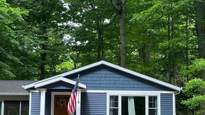 Ein Haus mit Veranda, einer amerikanischen Flagge und zwei grünen Adirondack-Stühlen.
