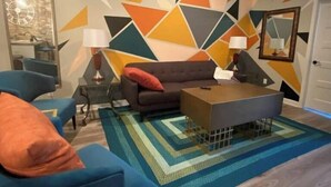 A modern living room with a geometric-patterned wall, a sofa, a coffee table, and blue armchairs. - Unique geometric shapes this Villa (Jeffersonville)