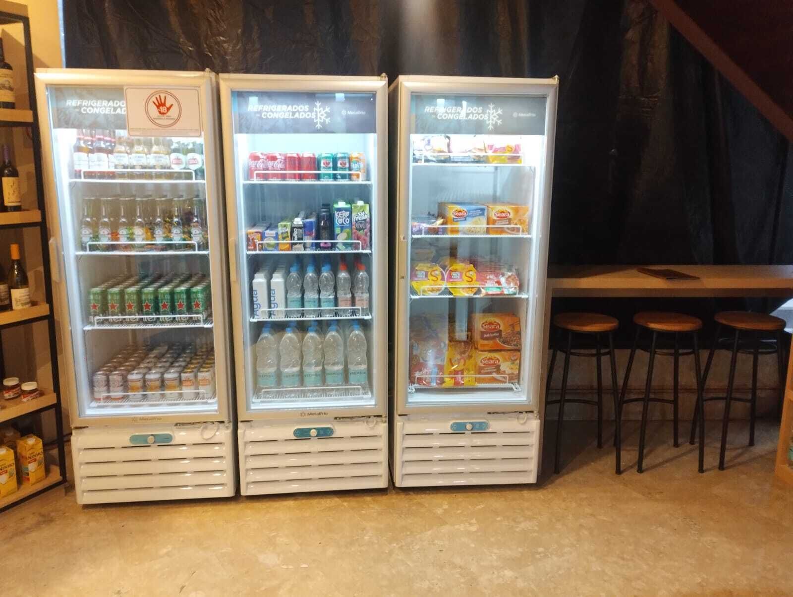Tres máquinas expendedoras blancas con puertas de vidrio, repletas de diversas bebidas y aperitivos.