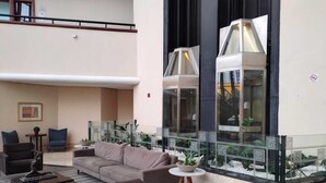 A spacious lobby with a high ceiling, a seating area with sofas and armchairs, and a glass enclosure with plants. - Summit Flat Service São José dos Campos (São José dos Campos)