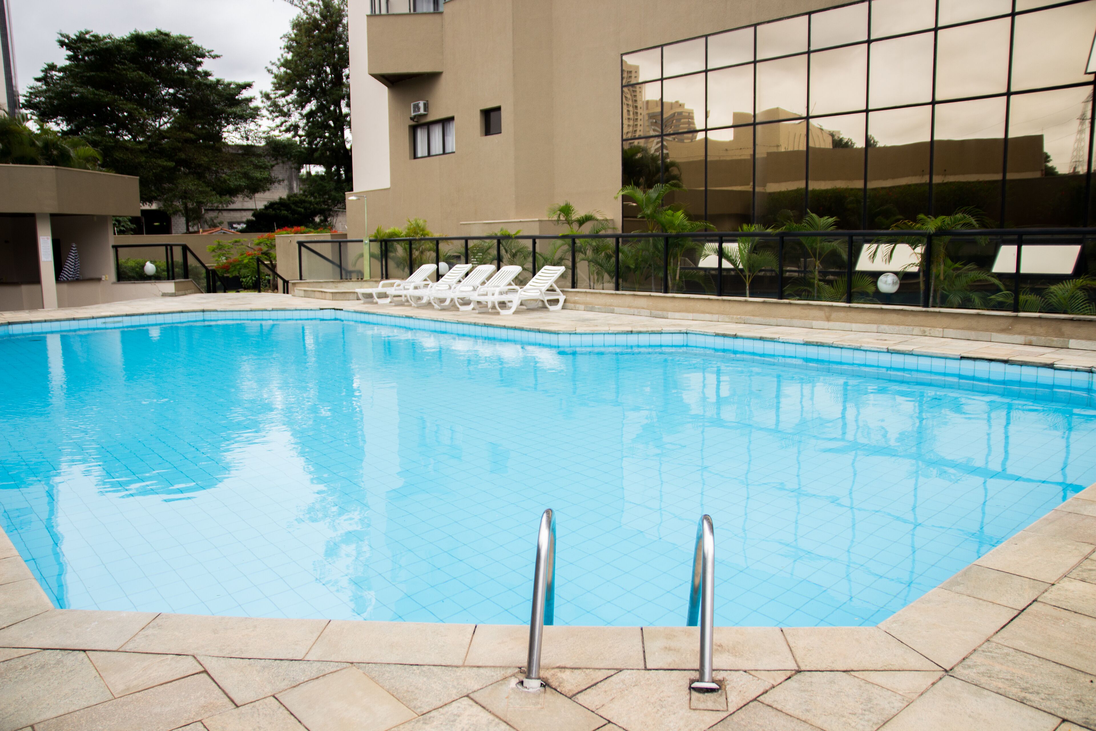 A swimming pool with clear blue water, surrounded by lounge chairs and a modern building with large windows.
